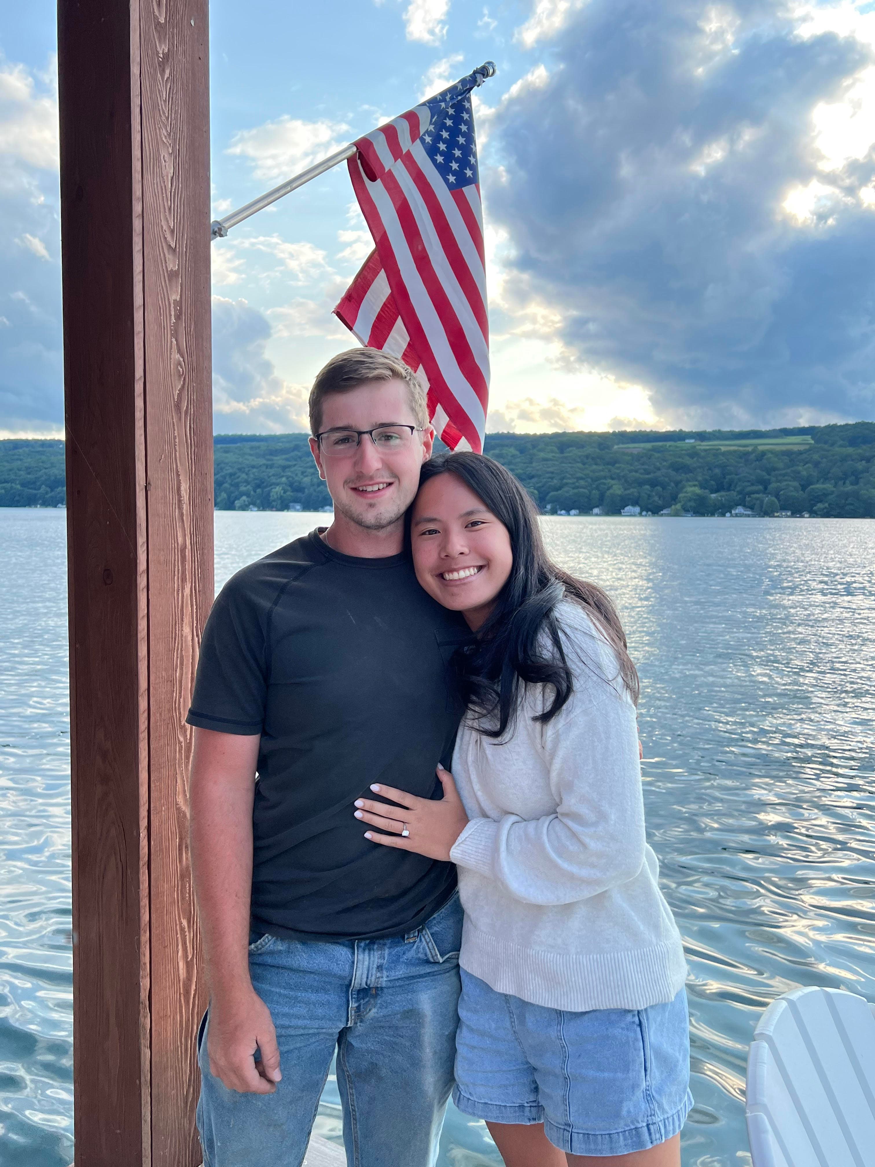 Young couple embracing on a dock with an American flag and Keuka Lake in the background