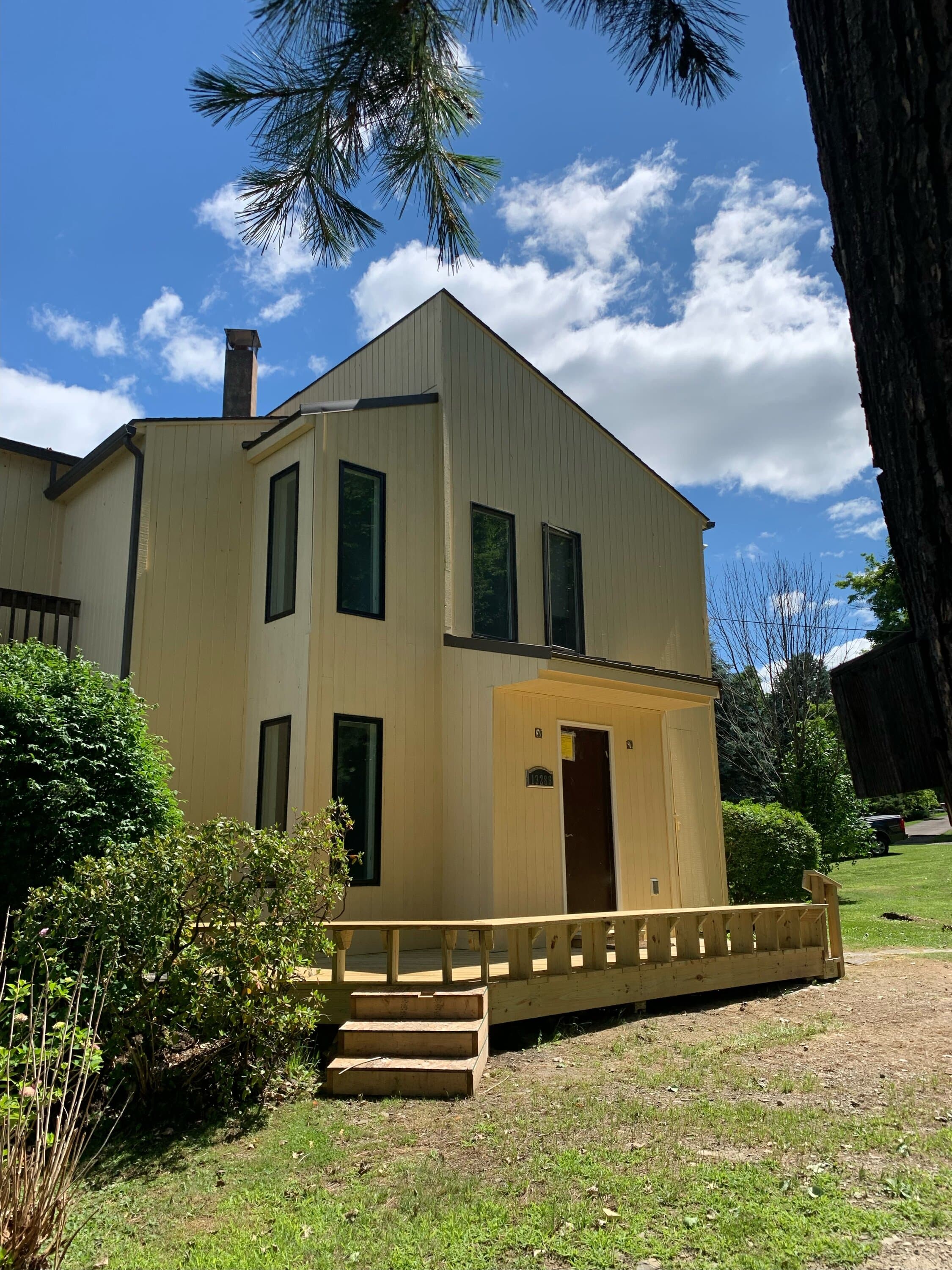 Two-story beige home with new wooden deck entrance and gabled roof