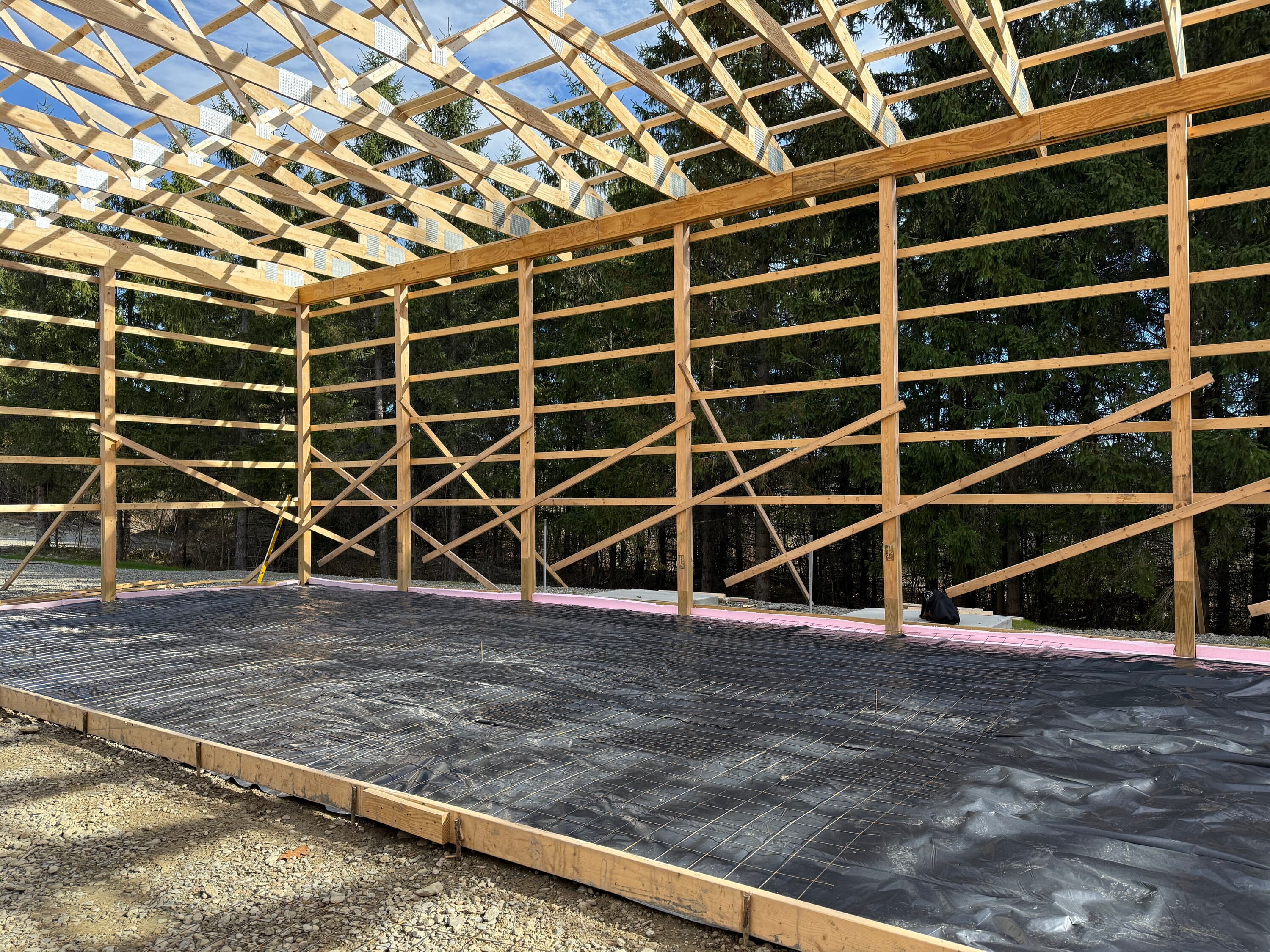 Wooden frame structure with roof trusses and black vapor barrier on foundation