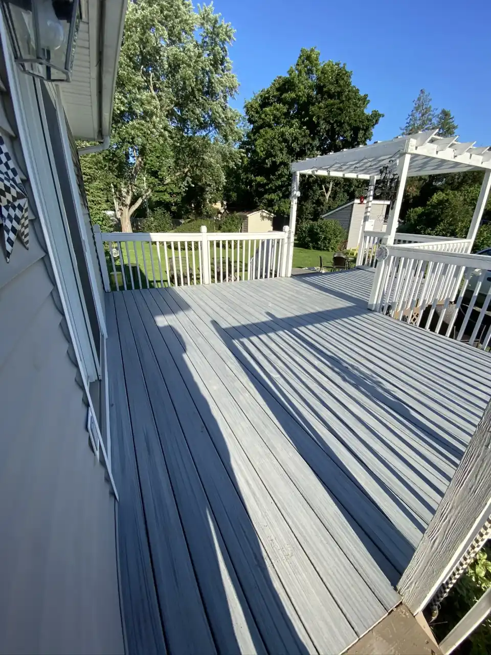 Gray composite deck with white railings and a white pergola overlooking the backyard